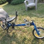Blauwe ligfiets met stuur onder de zitting in een tuin