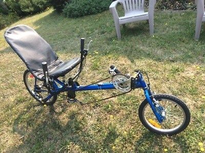 Blauwe ligfiets met stuur onder de zitting in een tuin